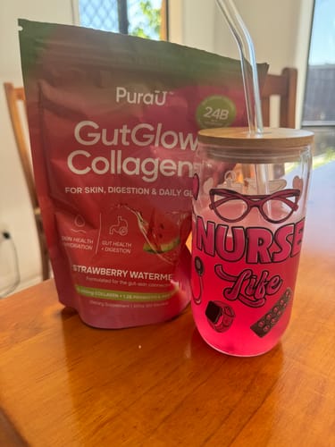 Reviewer's Strawberry Watermelon GutGlow Collagen pouch next to a glass of the prepared pink drink.