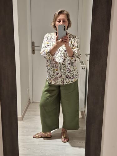 Cliente portant le pantalon Briac vert pomme avec une blouse fleurie et des sandales dorées.