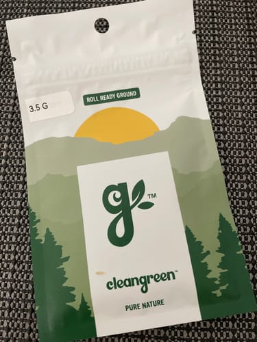 Customer's white and green pouch of Roll Ready Ground flower on a textured gray surface.