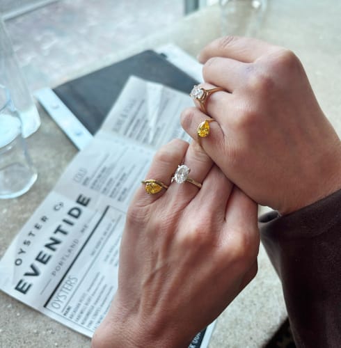 Customer's photo of two hands wearing matching Pia Birthstone Rings with yellow stones on the pinky fingers.