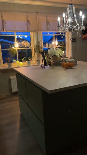 Anmelders kjøkkenøy med en benkeplate i Emmy beige kontaktplast sett i kveldslys foran et vindu.