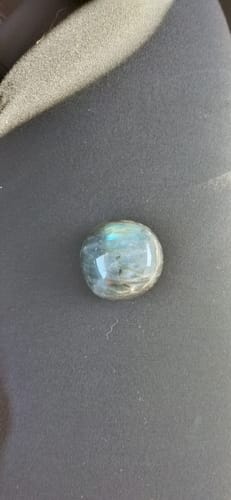 Reviewer's polished, circular monthly crystal showing blue iridescent flashes on a dark surface.