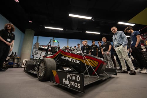 Customer's formula race car with a shiny red and yellow livery using the Liquid Metal Red wrap, viewed by a group indoors.