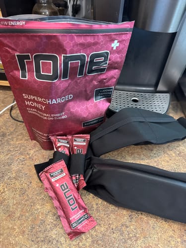 Customer's bag and single-serve packets of SuperCharged Honey on a counter next to a black running belt.