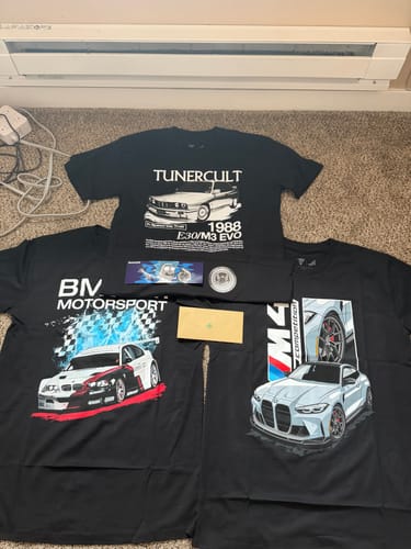 Customer's three black graphic T-shirts with car designs from the TCG93 MYSTERY CASH BOX laid out on a floor.