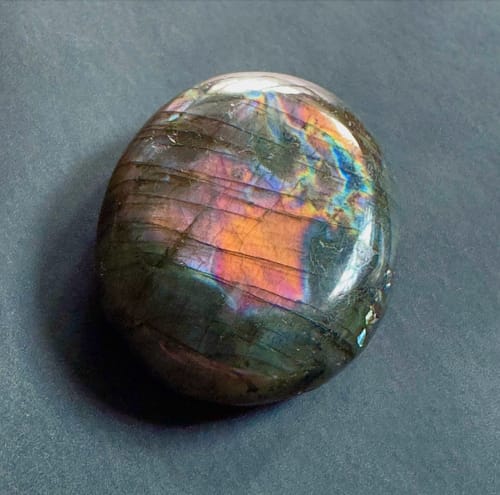 Reviewer's polished labradorite crystal with a vibrant orange, pink, and purple glow.