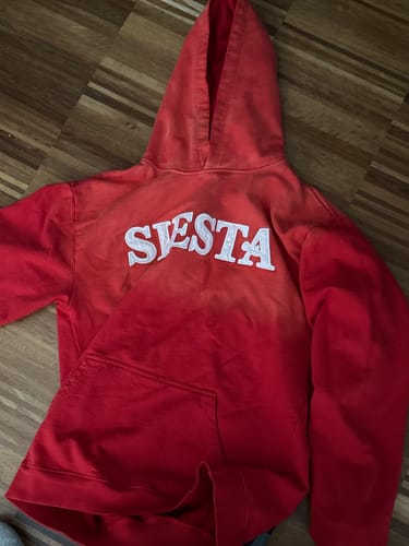 Customer's red LA SUDADERA: SIESTA hoodie laid flat, showing the white embroidered logo and sun-dry effect on the shoulders.