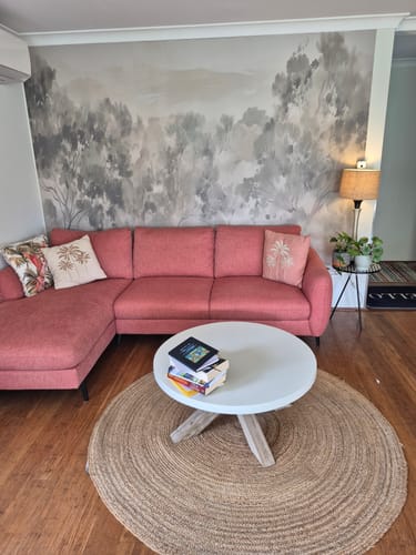 Customer's living room with Eucalyptus Haze Mural Wallpaper as a backdrop for a pink sectional sofa.