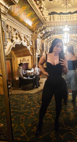 Customer taking a mirror selfie while wearing the black Naked Open Back Jumpsuit in an ornate room.