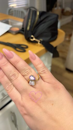 Customer's hand wearing the Navae Birthstone Ring, showing its shiny purple pear-cut and clear radiant-cut stones.