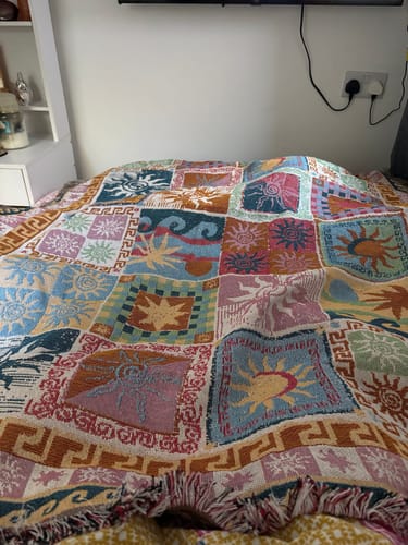 Customer's colorful Boho Tapestry Throw Blanket with a patchwork sun design spread across a bed.