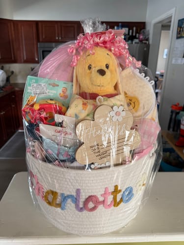 Customer's personalized knitted basket with 'Charlotte' in colorful yarn, filled with gifts and wrapped for a baby shower.