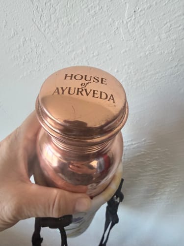 Close-up of a reviewer's hand holding the Pure Copper Water Bottle, with the brand logo visible on the lid.