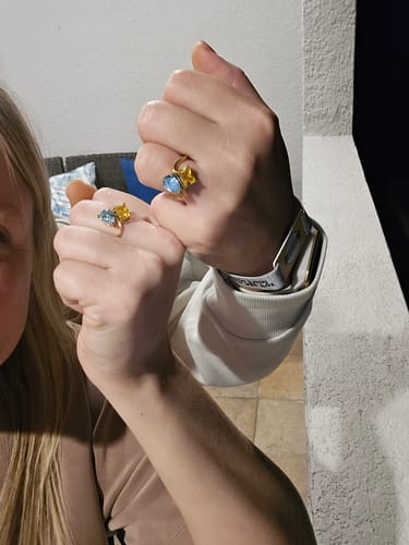 Two reviewers displaying their matching gold Navae Birthstone Rings with blue and yellow stones.