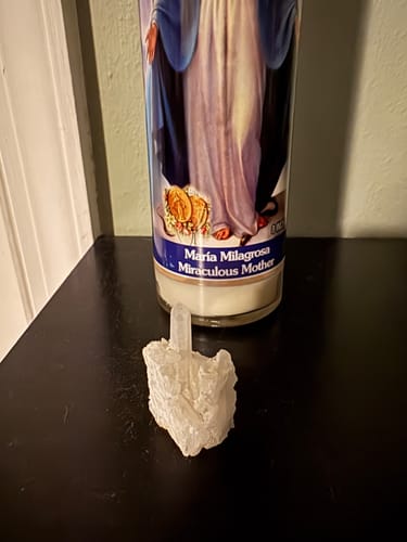 Customer's clear quartz crystal cluster sitting on a dark surface in front of a candle.