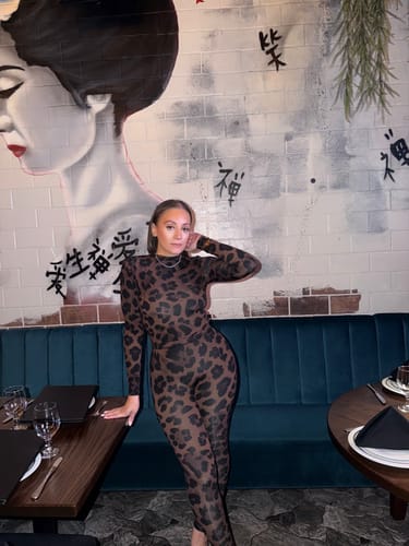 Customer posing in a restaurant wearing the Naked Print Bodysuit and matching leggings.