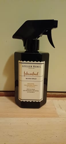 Recensent toont de zwarte fles van de Istanbul Room Spray op een houten ondergrond.