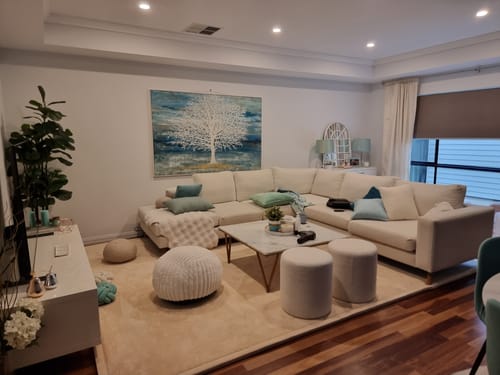 Customer's large beige Mellow Mat in a living room, placed under a sectional sofa and coffee table.