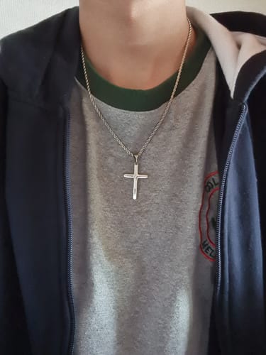 Primer plano de un cliente usando el colgante Crucifix Pendant sobre una camiseta gris.