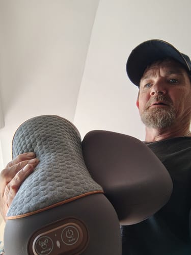 Reviewer holding the grey, textured Original Callixe Thera Pillow up close to the camera, showing its controls.