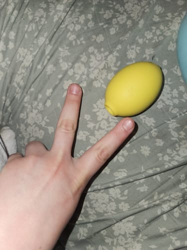 Reviewer making a peace sign next to their yellow Lem Clitoral Massager on a floral bedspread.