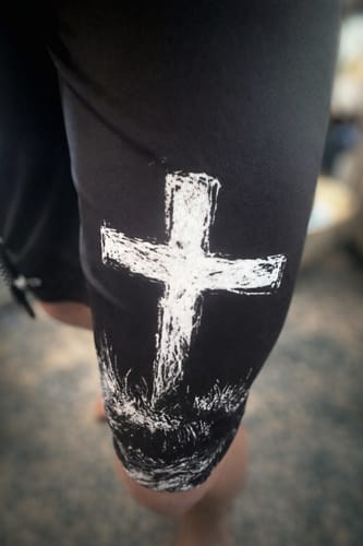 Close-up of a customer's black 'Cross' Youth Performance Shorts showing the white distressed cross graphic on the leg.