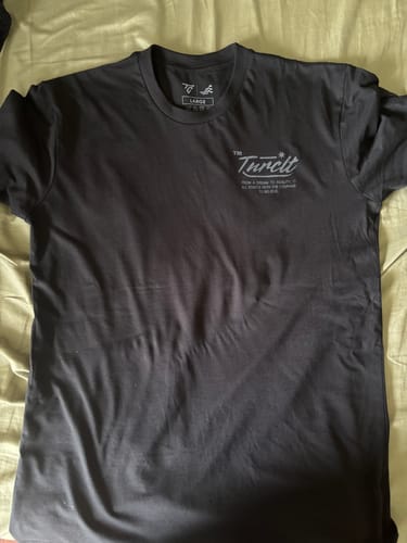 Customer's black MYSTERY TEE laid flat, showing the small logo on the front chest.