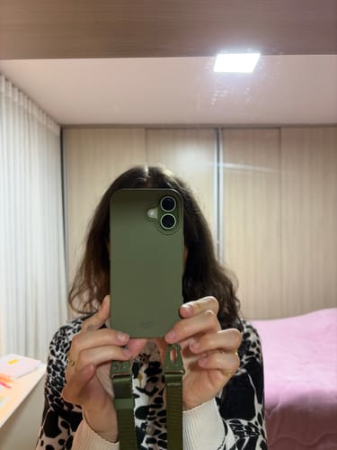 Cliente mostrando sua Case Verde Musgo em um celular, com uma alça da mesma cor conectada.