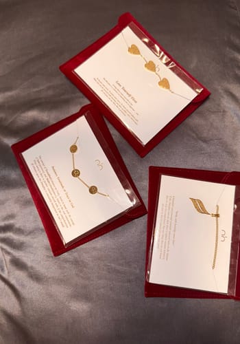 Customer's three different gold-colored necklaces, including the Hardship & Ease Necklace, in their red velvet packaging.