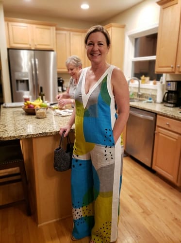 Customer smiling in a kitchen, wearing the loose, sleeveless printed jumpsuit with a deep V-neck.