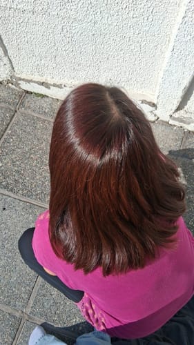 Una clienta muestra su cabello teñido con el Tinte Castaño, que se ve brillante y con un tono rojizo saludable a la luz del sol.