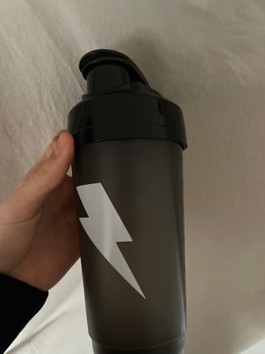 A reviewer's hand holding the dark shaker, showing the white lightning bolt logo.