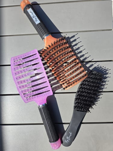 Photo d'une cliente montrant sa brosse démêlante format voyage avec deux autres brosses.