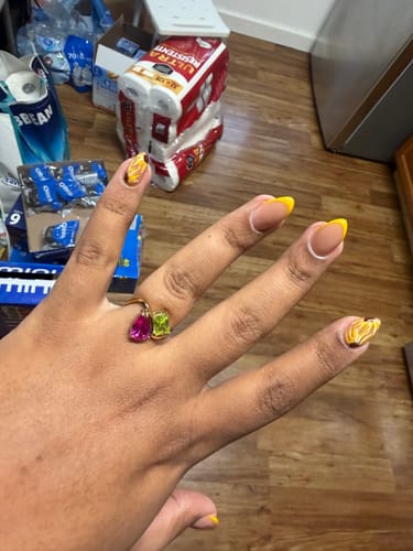 Customer's hand wearing the gold Navae Birthstone Ring with a pink pear-cut stone and a green radiant-cut stone.