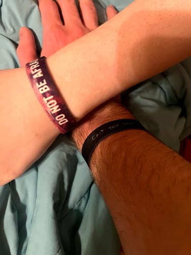 Customer wearing the black Cast Your Cares On Him bracelet, with their arm crossed beneath another person's arm.