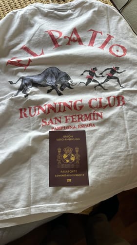 Reviewer's LA CAMISETA: SAN FERMIN t-shirt showing the 'Running Club' back graphic, with a Spanish passport placed on top.