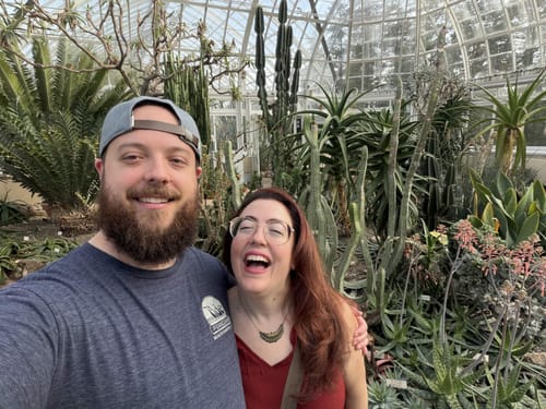 Reviewer wearing the Big Flat Bill Structured Canvas Hat backwards inside a sunny greenhouse.