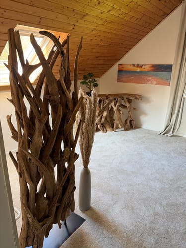 Kunde zeigt den Teak-Holz-Raumteiler RANTING als dekoratives Stück in einem Zimmer mit Dachschräge.