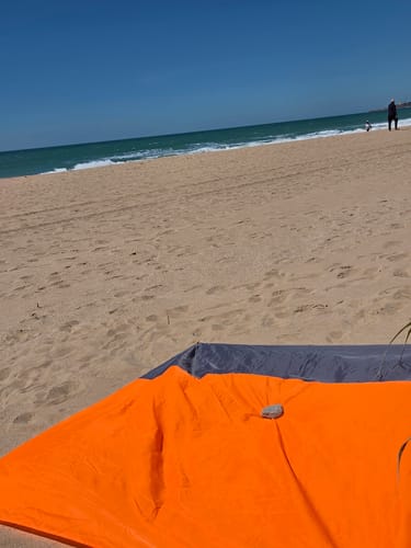 Kunde zeigt die orange-blaue Stranddecke am Sandstrand.