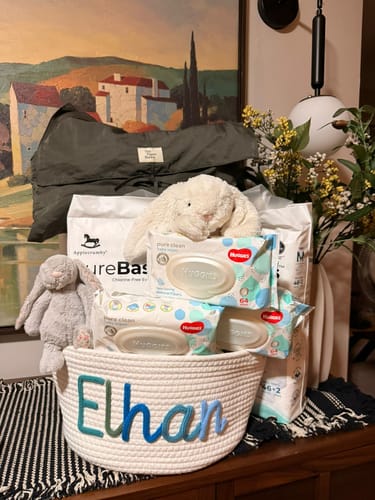 Customer's personalized knitted basket with the name 'Elhan' in multicolor yarn, filled with baby supplies for a gift.