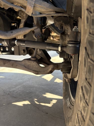 Reviewer's close-up of the new black Heavy Duty Tie Rod Kit installed on the undercarriage of a truck.