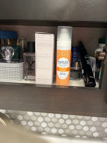 Reviewer's Florida Citrus Body & Hair Mist shown front and center in a medicine cabinet with other personal care items.