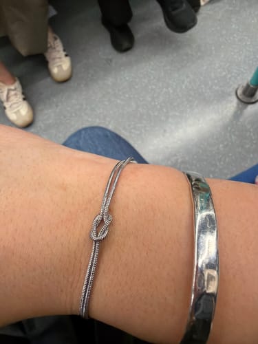 Customer wearing the shiny Forever Knot Bracelet on their wrist next to another bracelet.