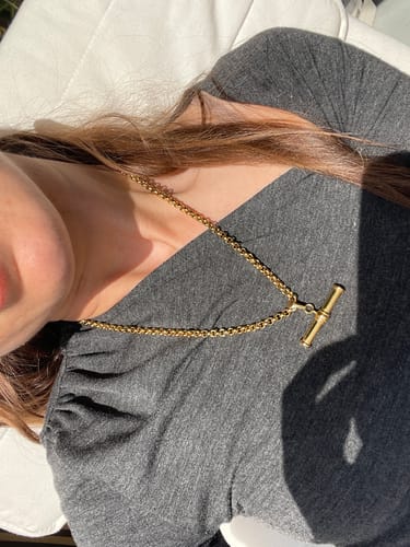 A customer wearing the gold XL T-Bar Necklace over a grey top, seen from above in the sunlight.