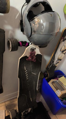 Reviewer's electric skateboard with Meepo Cyclone 107s wheels hanging on a wall next to a helmet.