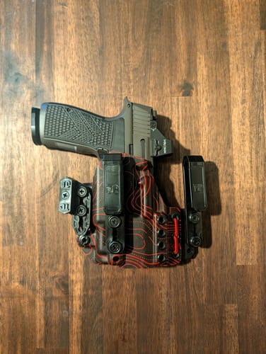 Customer's red and black patterned XIPHOS ELITE holster with a handgun inside, shown on a wooden surface.