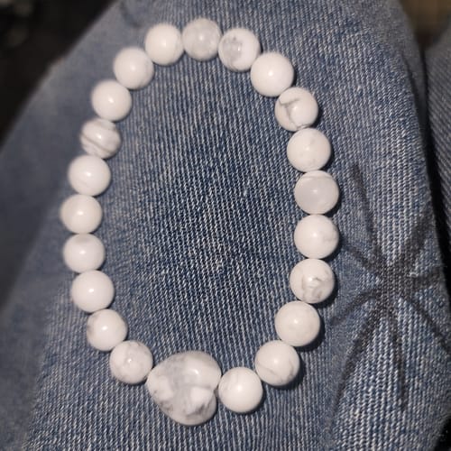 Reviewer's white howlite bracelet with a heart-shaped bead, shown resting on a denim surface.