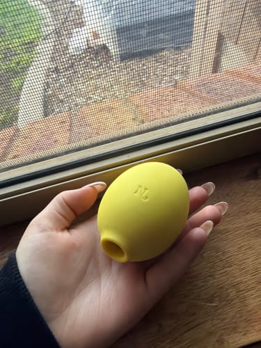 Customer holding the yellow Lem Clitoral Massager in their hand in front of a window.