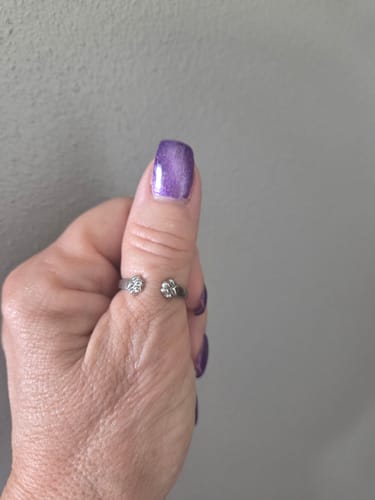 A reviewer's hand wearing the silver Paw Hug Ring on their thumb, showing the open design with two paw prints.