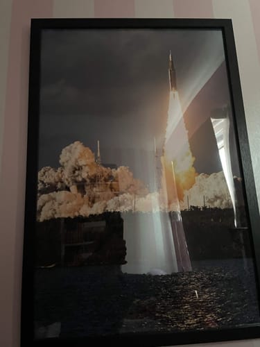 Customer's framed 'Full Send It! - SLS' print of a rocket launch hanging on a striped wall.